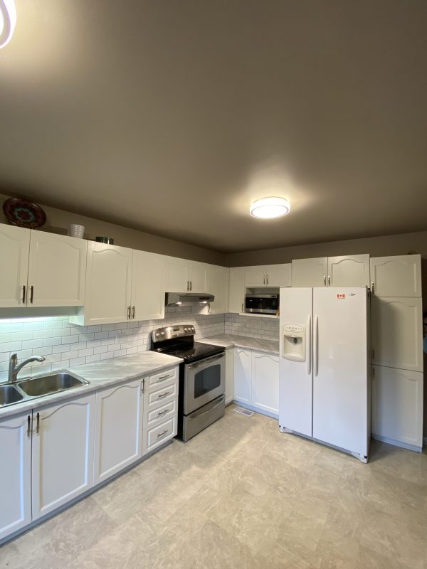 Freshly painted white cabinets in a modern kitchen with a tile backsplash.